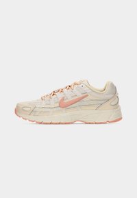 Cream and peach Nike sneaker with textured sole and laces, captured mid-air above a stone surface and concrete background.