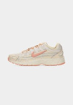 Cream and peach Nike sneaker with textured sole and laces, captured mid-air above a stone surface and concrete background.